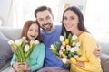 Photo of happy family hug cuddle enjoy time together positive smile girls hold flowers bouquet spring sit couch home