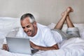 Happy middle aged man using laptop while lying in bed at home Royalty Free Stock Photo