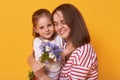 Photo of happy mother and kid. Affectionate female holds on tight her little charming daughter. Cute child gives bouguet of