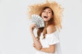 Photo of happy rich woman 20s wearing big straw hat rejoicing while demonstrating fan of dollar cash, isolated over white