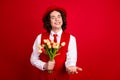 Photo of happy teenage boyfriend wearing formal suit gives you a hand invitation event and bunch tulips isolated on red