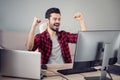 Photo of happy victorious young man raise fists sit desk look computer software designer indoors inside office