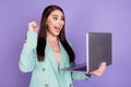 Photo of happy victorious young woman raise fist look laptop victory amazed isolated on purple color background