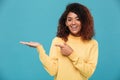 Happy young african lady dressed in warm sweater pointing.