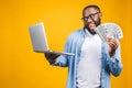 Photo of happy young afro american handsome man posing isolated over yellow wall background using laptop computer holding money Royalty Free Stock Photo