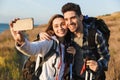 Happy young loving couple outside with backpack in free alternative vacation camping take selfie by mobile phone