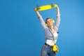 Photo of happy young woman hold yellow penny or skateboard dancing over blue background.