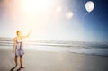 Happy young woman letting go of balloons on beach