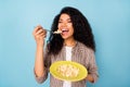 Photo of hungry charming dark skin woman dressed checkered shirt eating cornflakes closed eyes isolated blue color