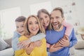 Photo of idyllic family mom dad hug piggyback two adorable kids boy girl in house indoors