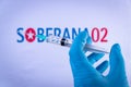 In this photo illustration a hand in medical gloves holds a syringe in front of Soberana 02 vaccine logo in Barcelona, Spain on Se