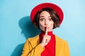 Photo of impressed cute young lady wear yellow blazer red cap finger lips asking keep silence isolated blue color