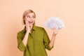 Photo of impressed ecstatic woman with bob hairdo dressed green shirt staring at money palm on cheek isolated on beige Royalty Free Stock Photo