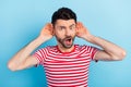 Photo of impressed furious young man dressed striped t-shirt arms ears listening secrets isolated blue color background