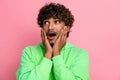 Photo of impressed speechless curly funny indian man in green sweatshirt touch cheeks look empty space isolated on pink