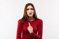 Photo of indignant brunette female in casual red sweater pointing finger at herself. Studio shot, white background