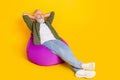 Photo of inspired mature man sit beanbag hands behind head sleep wear green shirt isolated yellow color background Royalty Free Stock Photo