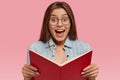 Photo of intelligent European female wonk holds opened book, feels happy to read romantic story to end, feels excited