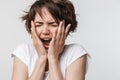 Photo of intimidated woman with short brown hair in basic t-shirt keeping hand over her face and screaming at camera Royalty Free Stock Photo