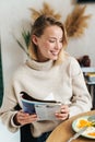 Photo of joyful blonde woman reading magazine while having breakfast Royalty Free Stock Photo