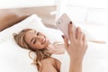 Photo of joyful caucasian woman smiling and using cellphone while lying Royalty Free Stock Photo