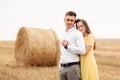 Photo of joyful couple man and woman walking through golden field with bunch of haystacks and hugging together during sunny day Royalty Free Stock Photo