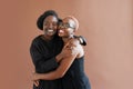 Photo of joyful dark skinned women dressed casually, smile positively, stand against brown background