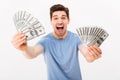 Photo of joyful man in casual t-shirt screaming and demonstrating his money prize in dollar cash on camera, isolated over white w