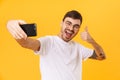 Photo of joyful young man taking selfie and showing thumb up