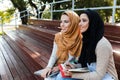 Photo of joyous islamic girls wearing headscarfs sitting on bench in park Royalty Free Stock Photo