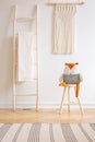 Real photo of a ladder with a blanket, toy on a chair and macrame on a wall in a natural kid room interior