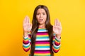 Photo of little afraid girl raise two palms show refusal wear striped shirt isolated yellow color background