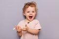 Photo of little cute child girl holding toothbrush, trying brushing teeth herself at morning every day, standing isolated on gray Royalty Free Stock Photo