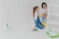 Photo of little girl and her mum paint furniture for new apartment, pose in empty room, use color samples, use painting tools, Royalty Free Stock Photo