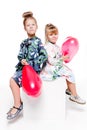 2 little girls with elegant dresses sit with large bags with heart-shaped balloons inside Royalty Free Stock Photo