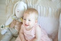 Little happy girl sitting near bed with toy rabbit