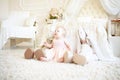 Little sad girl sitting between toy rabbits near bed