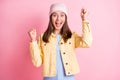 Photo of lucky charming young woman dressed casual clothes cap rising fists open mouth isolated pink color background