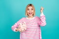 Photo of lucky excited girl dressed striped sweater rising fist money box isolated teal color background Royalty Free Stock Photo