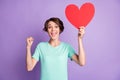 Photo of lucky young woman dressed casual turquoise clothes holding pointing big red heart arm fist isolated violet Royalty Free Stock Photo