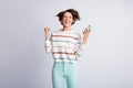 Photo of lucky young woman dressed striped pullover holding modern gadget rising fist closed eyes isolated grey color