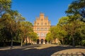 Photo of main building of University from entrance gate on blue autumn sky and yellow and green foliage on trees. Architecture of