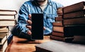 Photo of male person holding smartphone amidst old books