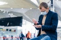 Photo of man in medical face mask, uses disinnfectant spray for hands, protects from coronavirus in crowded place, poses in