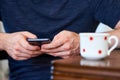 Photo of a man`s hand holding a cell phone. He is sitting in the interior of the apartment and writing a text message on the Royalty Free Stock Photo