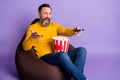 Photo of man sit beanbag hold remote control box popcorn wear yellow sweater jeans isolated purple background