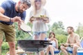 Man using bellows for preparing food in barbecue grill with friends on pier