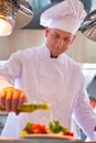 Mature chef using pouring oil on salad in plate at restaurant