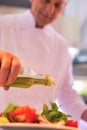 Mature chef using pouring oil on salad in plate at restaurant