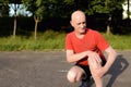 Photo of mature, elderly man sitting in the park and touching his knee by the pain during the day. Royalty Free Stock Photo